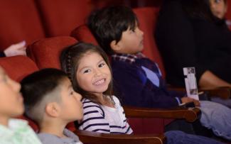 Child in audience of Civic Theatre, smiling at camera