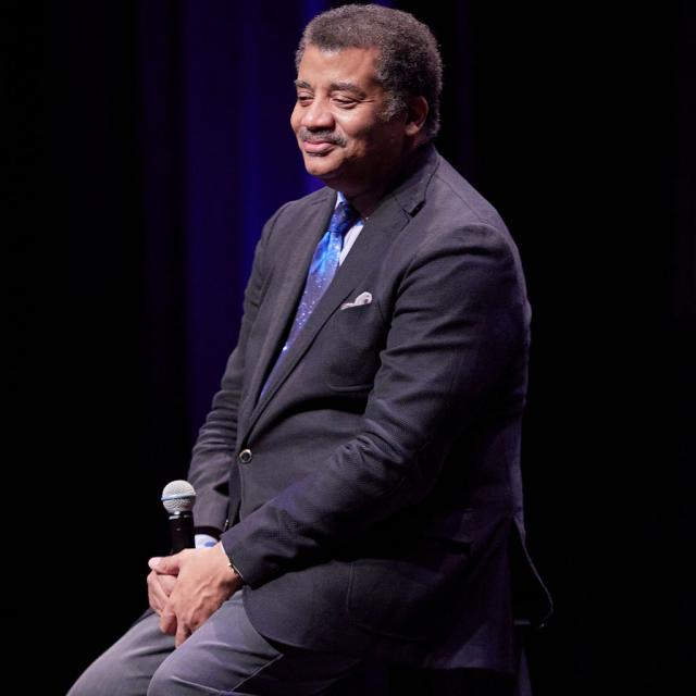 Dr. Neil DeGrasse Tyson looking offstage, smiling, microphone in hand